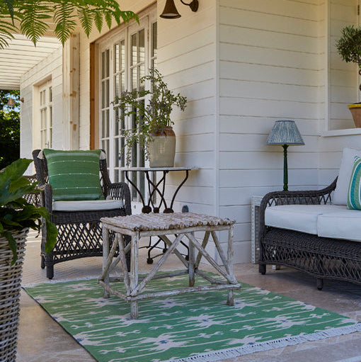 Outdoor patio area with wicker furniture, cushions, and potted plants on a porch.