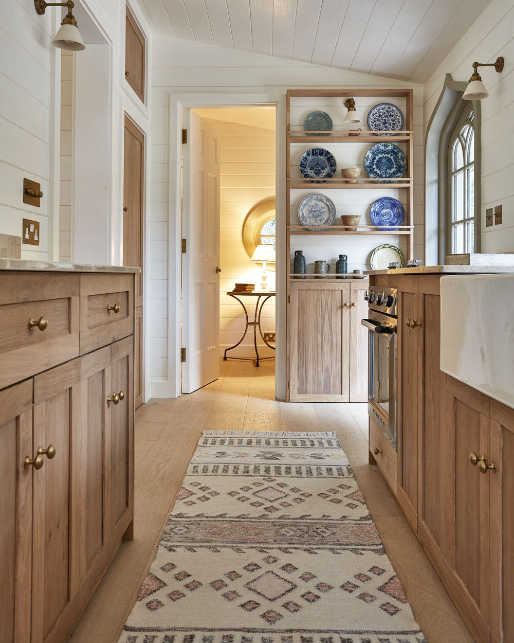 Kitchen with wooden cabinets, a patterned rug, and decorative plates on shelves.