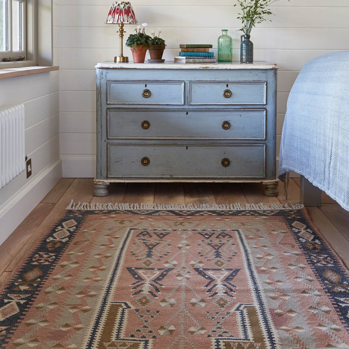 Vintage-style dresser with decorative items in a room with a patterned rug and framed picture on the wall. *collection_bedroom-rugs