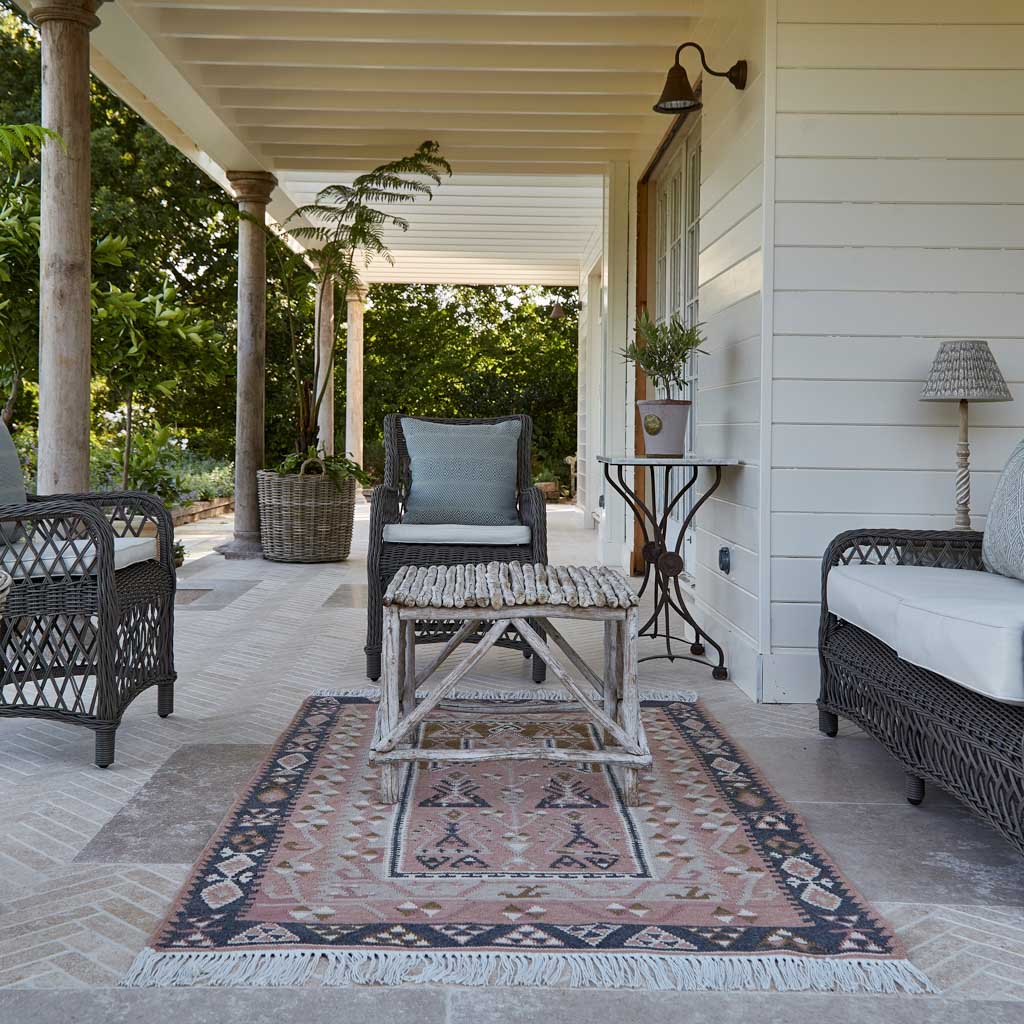 Outdoor patio with wicker furniture, table, and rug on a porch.