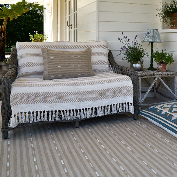 Outdoor patio with wicker loveseat, striped blanket, and decorative pillows on a patio floor.