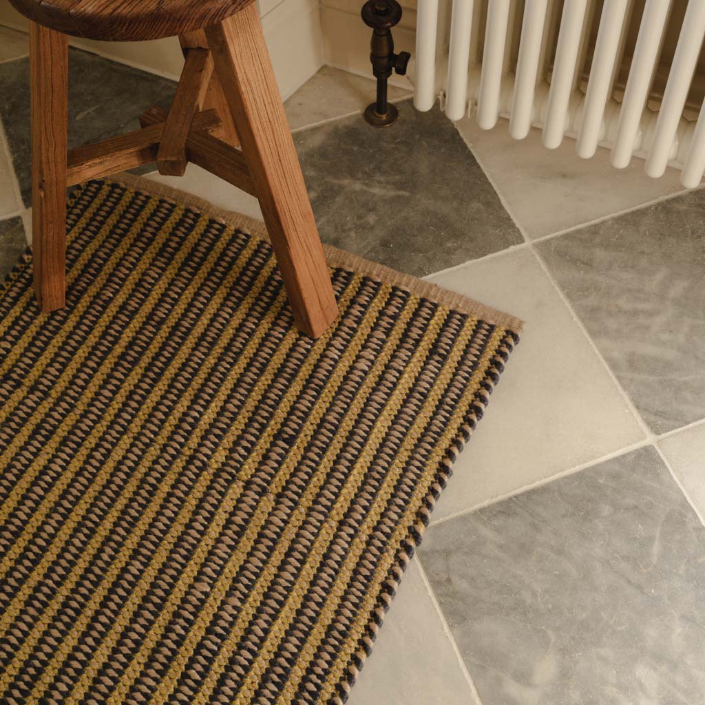 Textured rug on a tiled floor with a wooden stool and radiator in the background