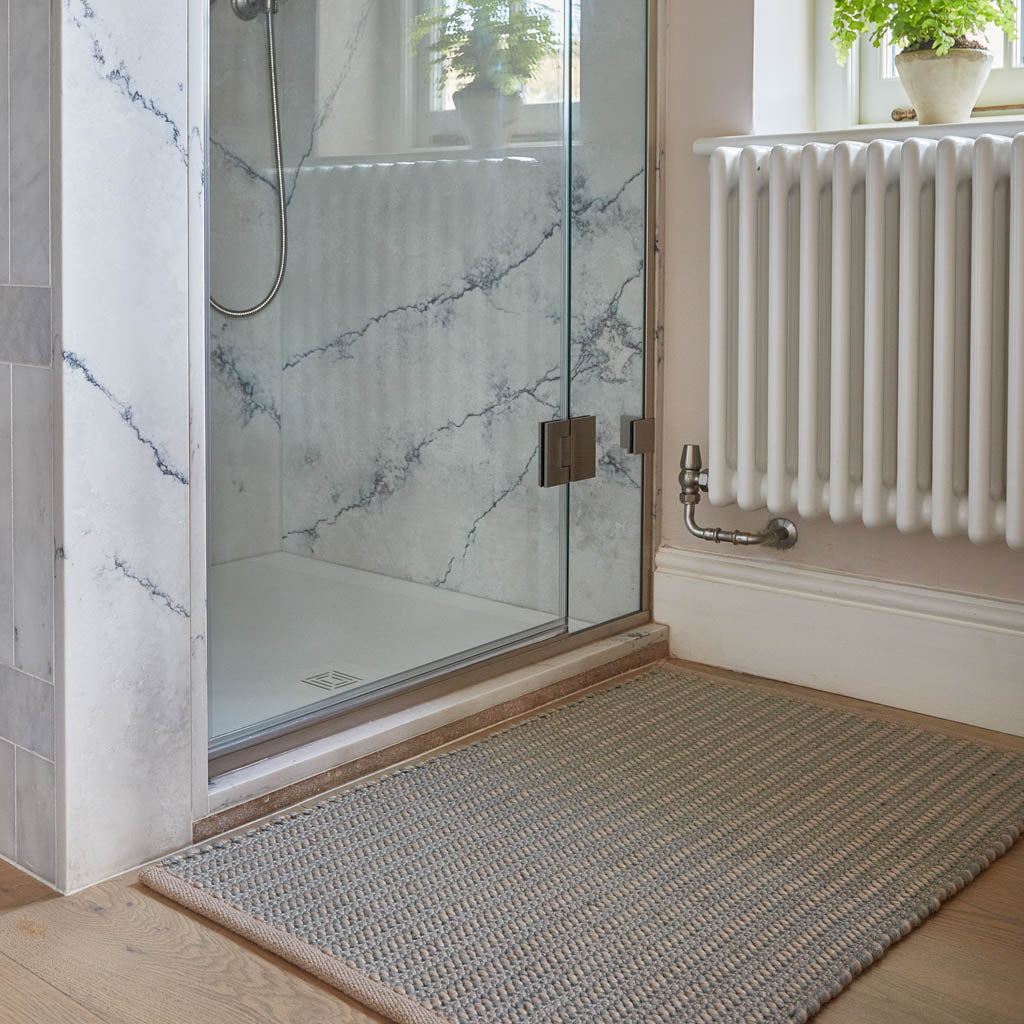 A sky blue rug with subtle grey and beige detailing, placed on a floor beside a shower enclosure and a white radiator.