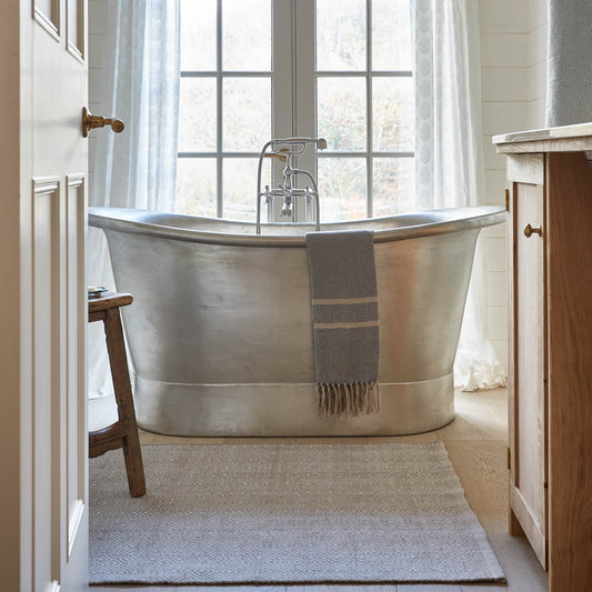 A Chinchilla Diamond Rug placed on the floor in front of a bathtub, with soft natural lighting from a nearby window.