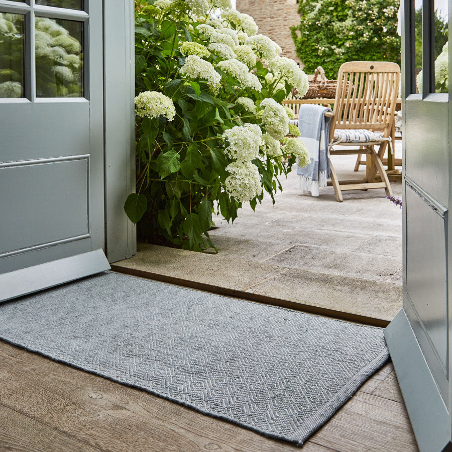 A dove grey rug with a subtle diamond pattern, used as a doormat