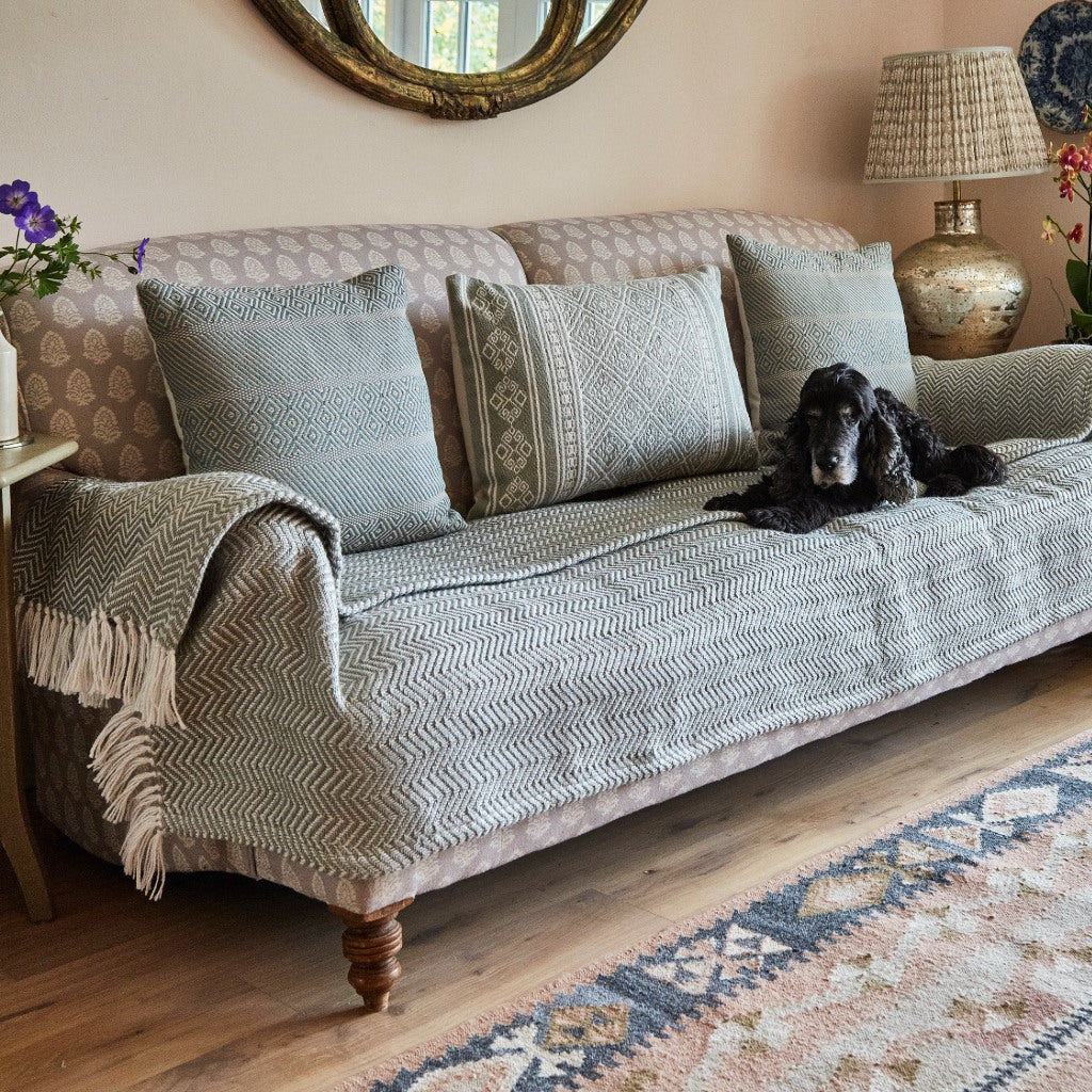 Dog lying on a patterned sofa with cushions and a grey herringbone blanket in a cozy living room. *collection_sofablanket