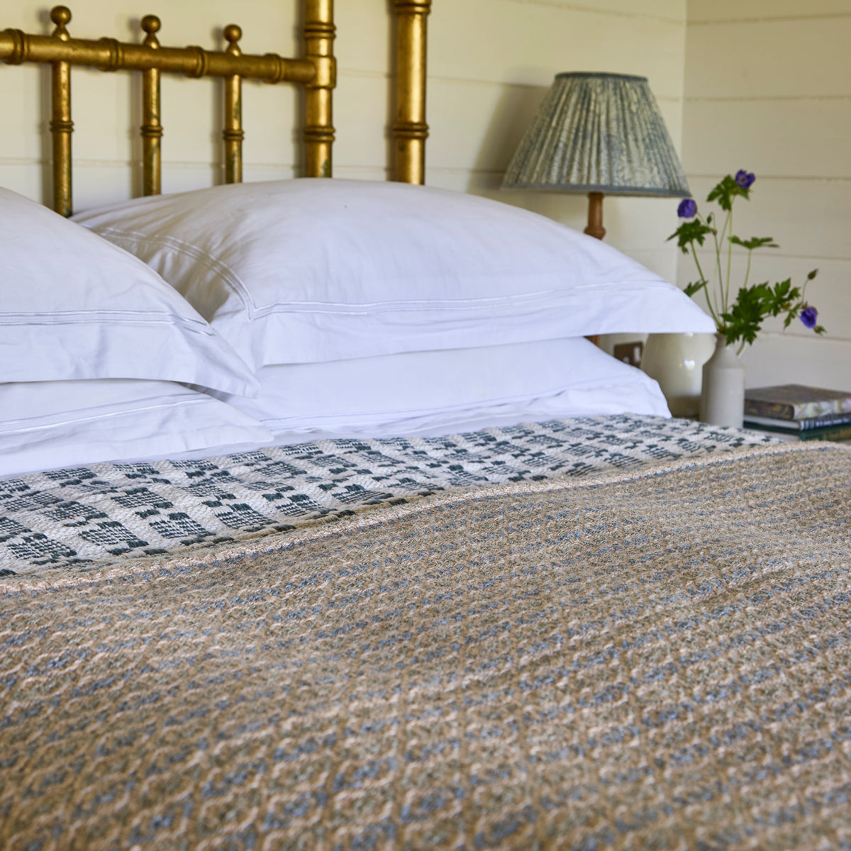Bed with white pillows, a patterned blanket, and a lamp on a nightstand.
