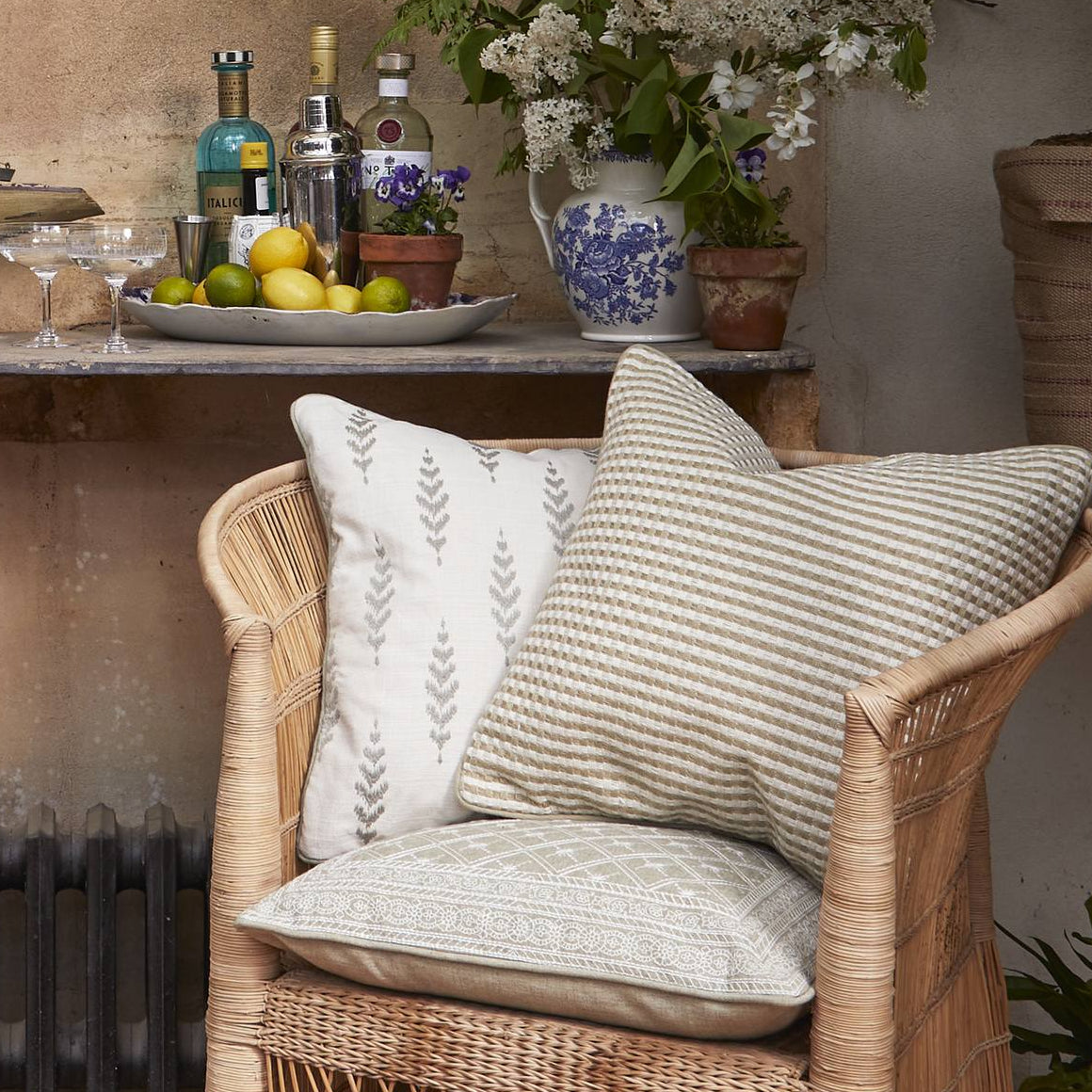 Cozy outdoor seating area with a wicker chair, lantern, and decorative items on a striped rug. *collection_outdoor