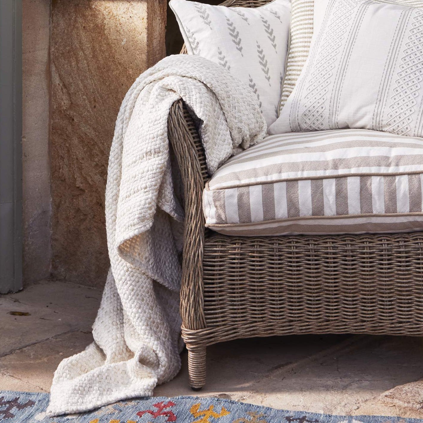 Wicker chair with striped cushions and a blanket on a colorful rug in a sunroom. *collection_outdoor