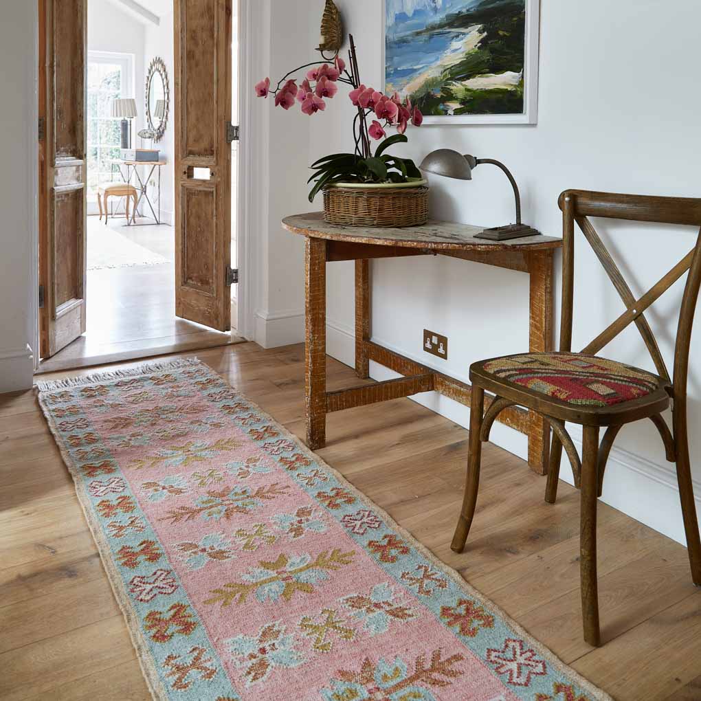 A pink, pale blue and neutral coloured rug in a hallway