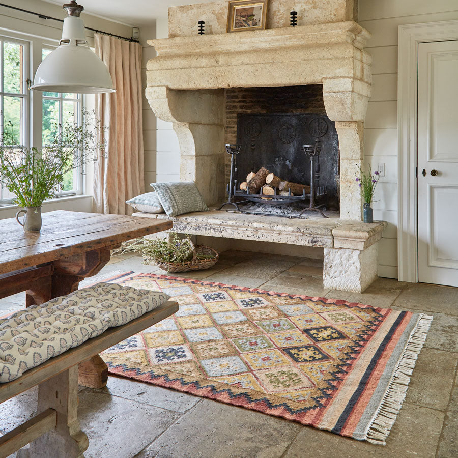 Geometric patterned rug in neutral brown, olive and yellow tones next to a fireplace