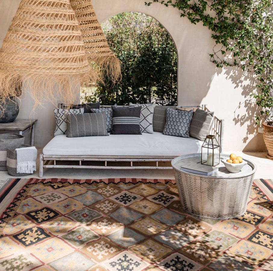 A traditional Nomad Xanthos rug with a geometric pattern laid out on a patio area, complementing the outdoor furniture and decor.