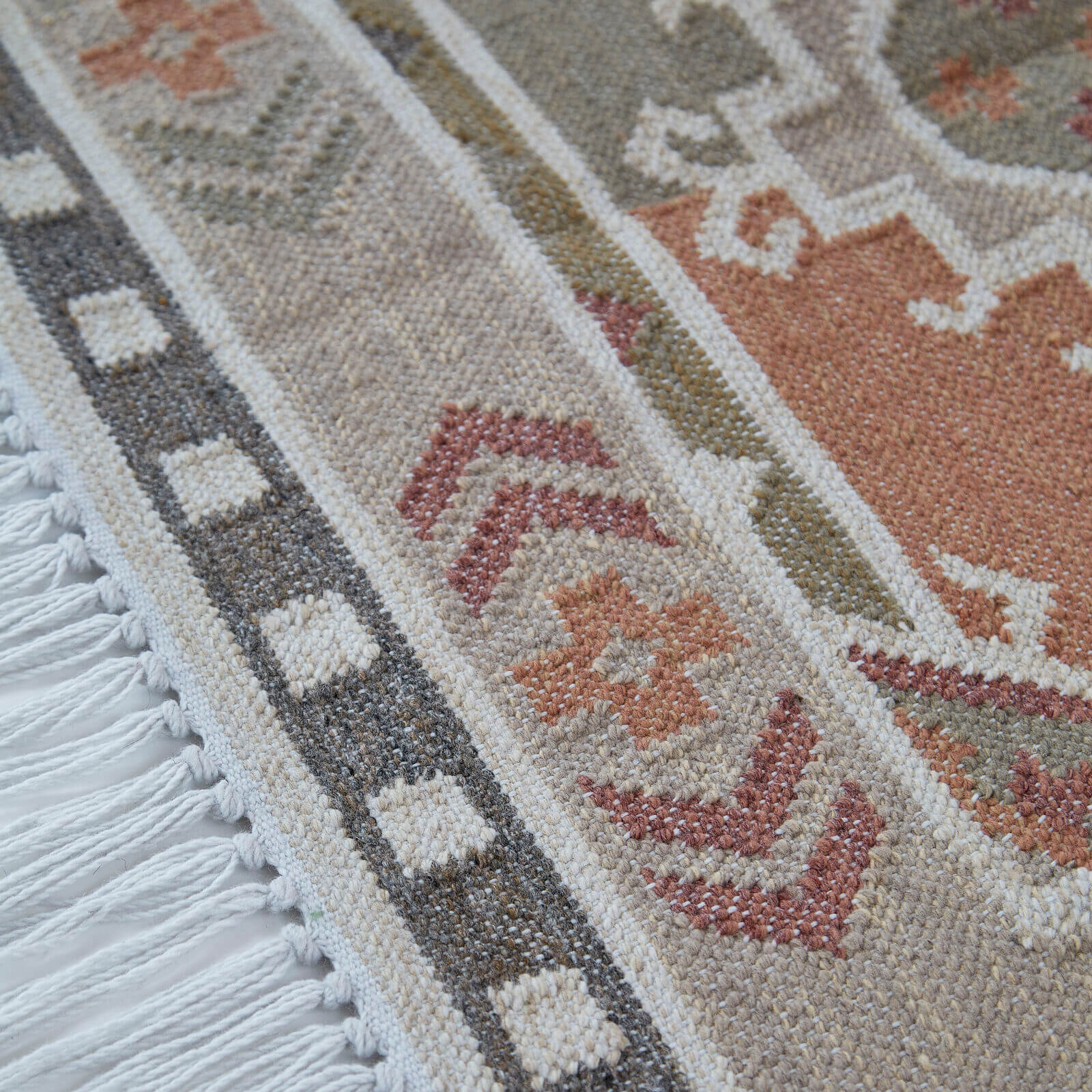 Close-up of a neutral patterned rug with geometric designs and fringes.