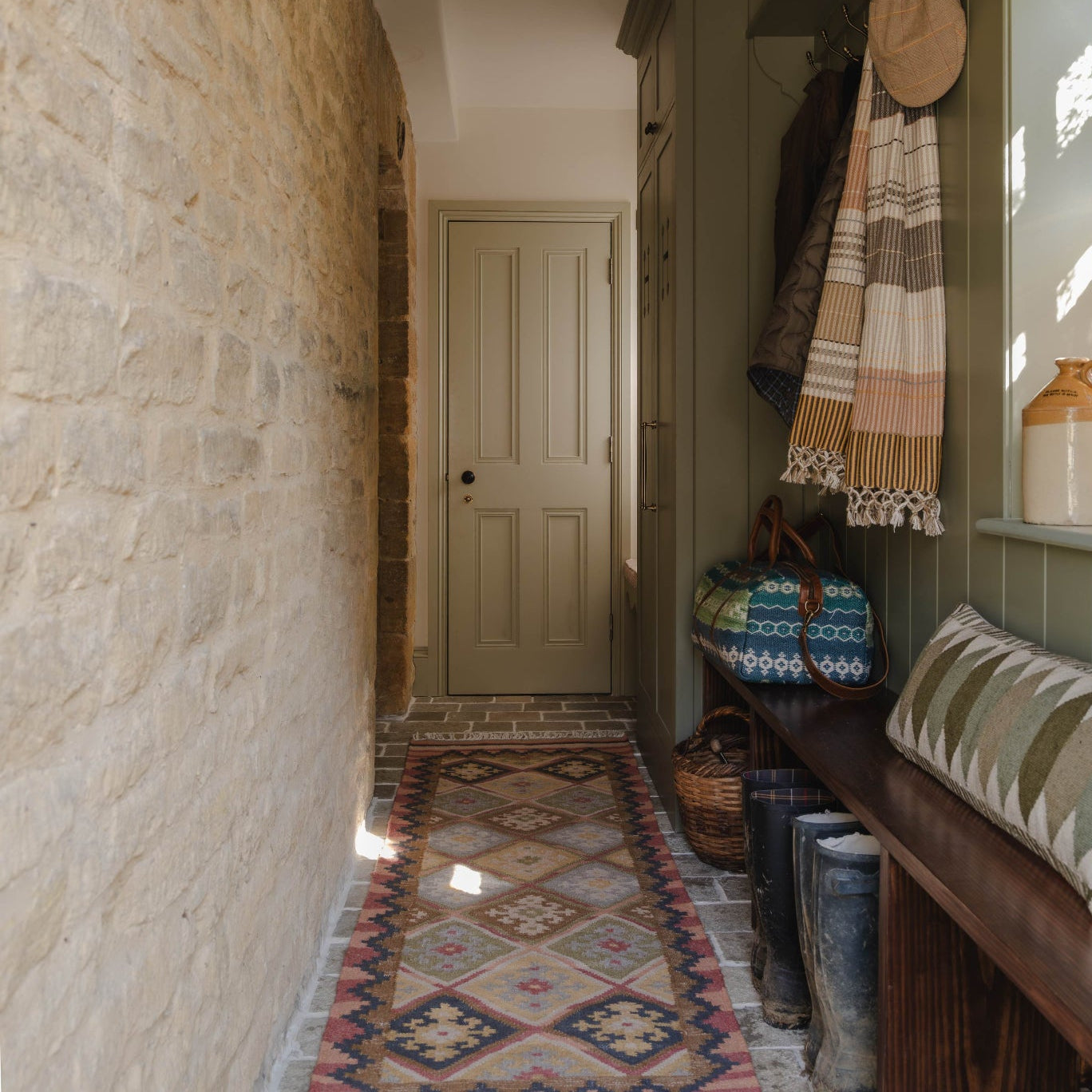 Narrow hallway with stone walls, patterned kilim rug, and wooden bench.