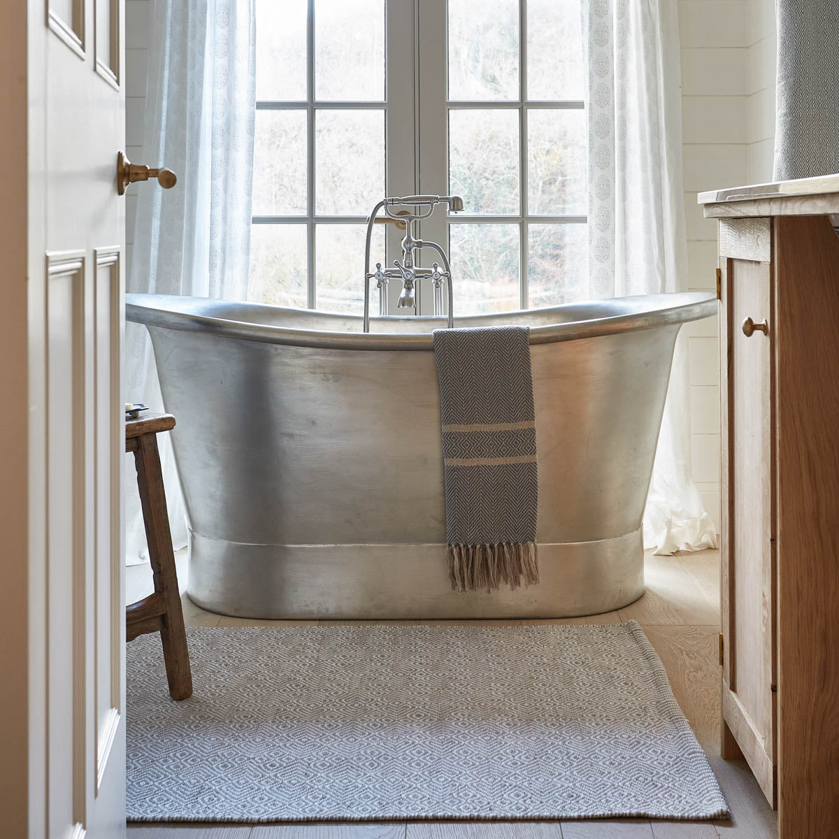 A gray Chinchilla Provence Rug placed on the floor in front of a bathtub, with a doormat visible to the left.