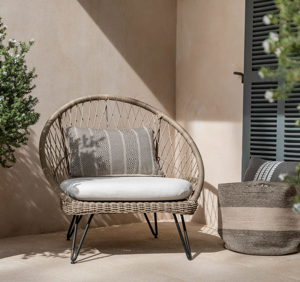 Wicker chair with cushions on a patio with a neutral wall and plant in the background