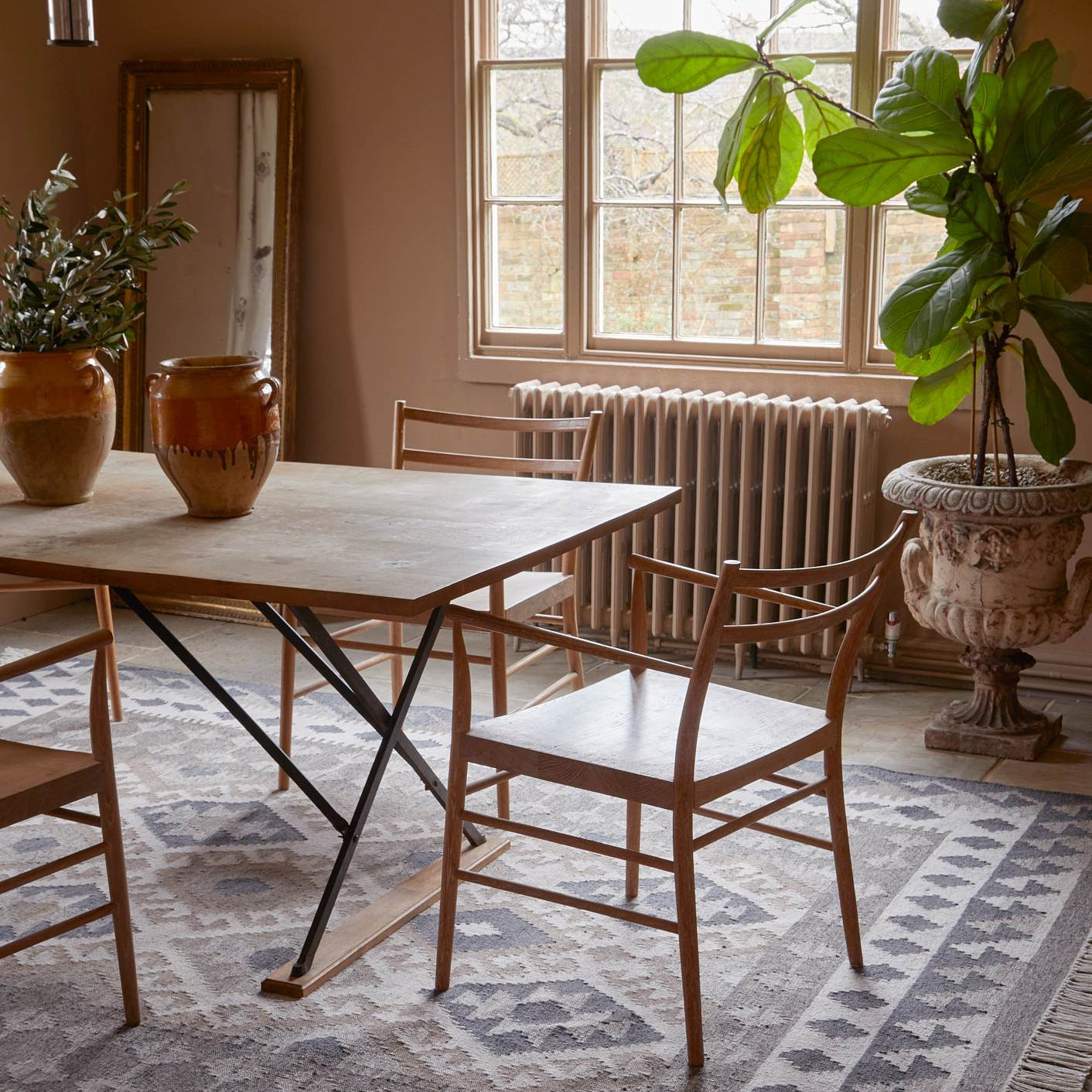 Dining room with wooden table, chairs, and plants on a patterned rug.