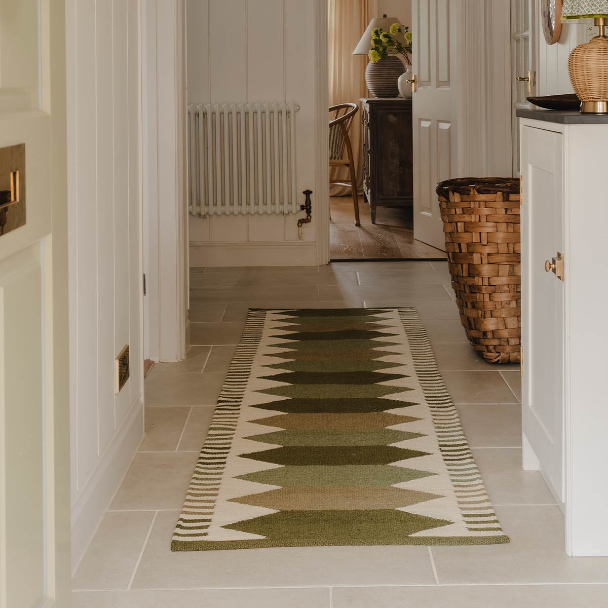 Green geometric patterned kilim runner rug on a tiled floor, with a door at the far end leading to another room. *collection_hallway-rugs