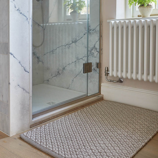 A gray rug with diamond geometric pattern placed on a floor, likely in a home environment.