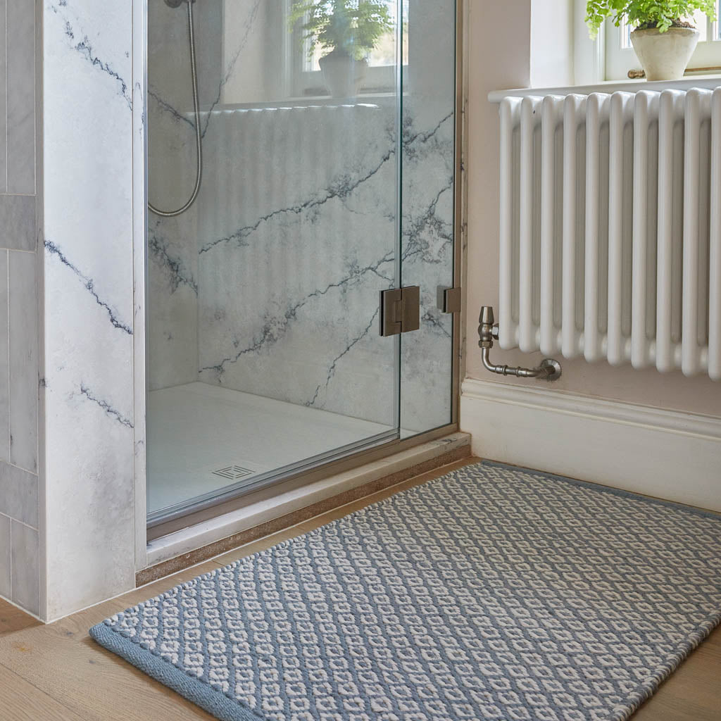 A sky blue rug with a geometric diamond pattern placed on a floor next to a shower door.