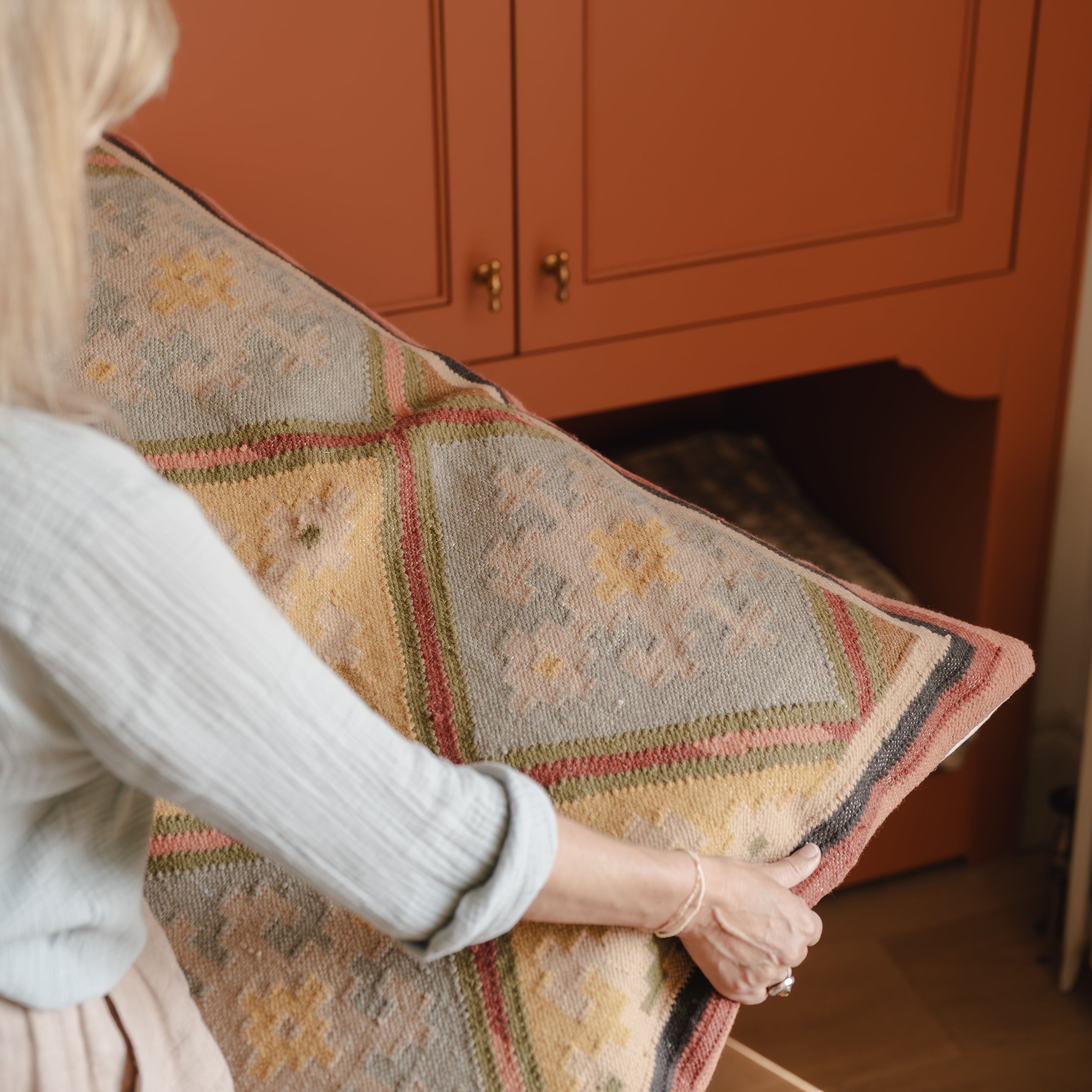 Person holding a decorative pillow in front of an orange cabinet.