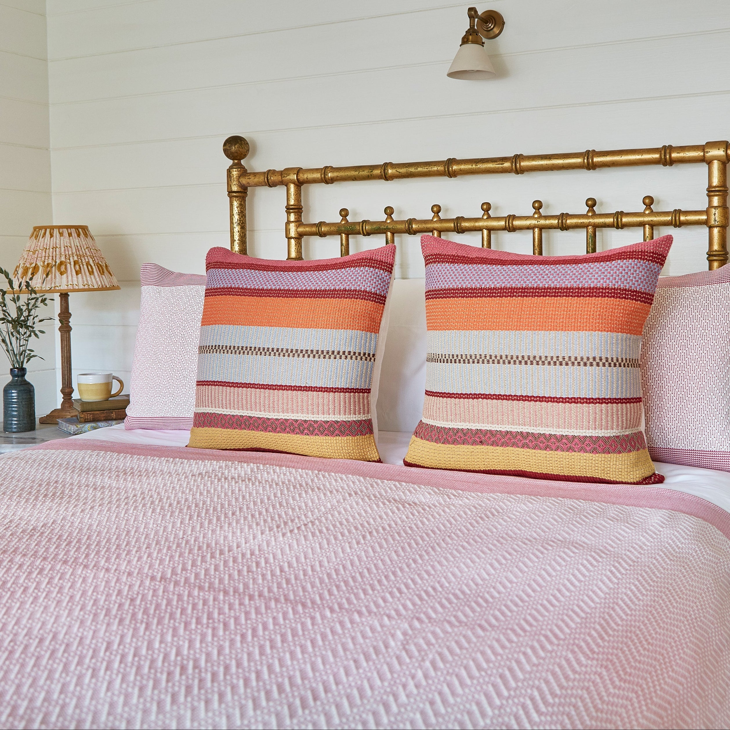 Bedroom with a bed featuring pink bedding and striped pillows, flanked by two lamps on nightstands.
