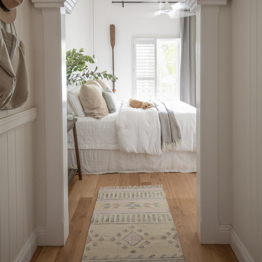 Bedroom with a bed, and a pink and cream kilim rug, and plant in a home interior setting.