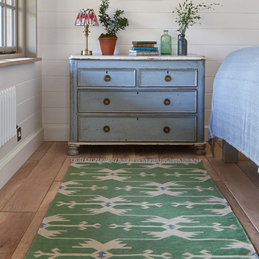 A green geometric patterned rug with traditional motifs placed in a room setting, complementing the decor.