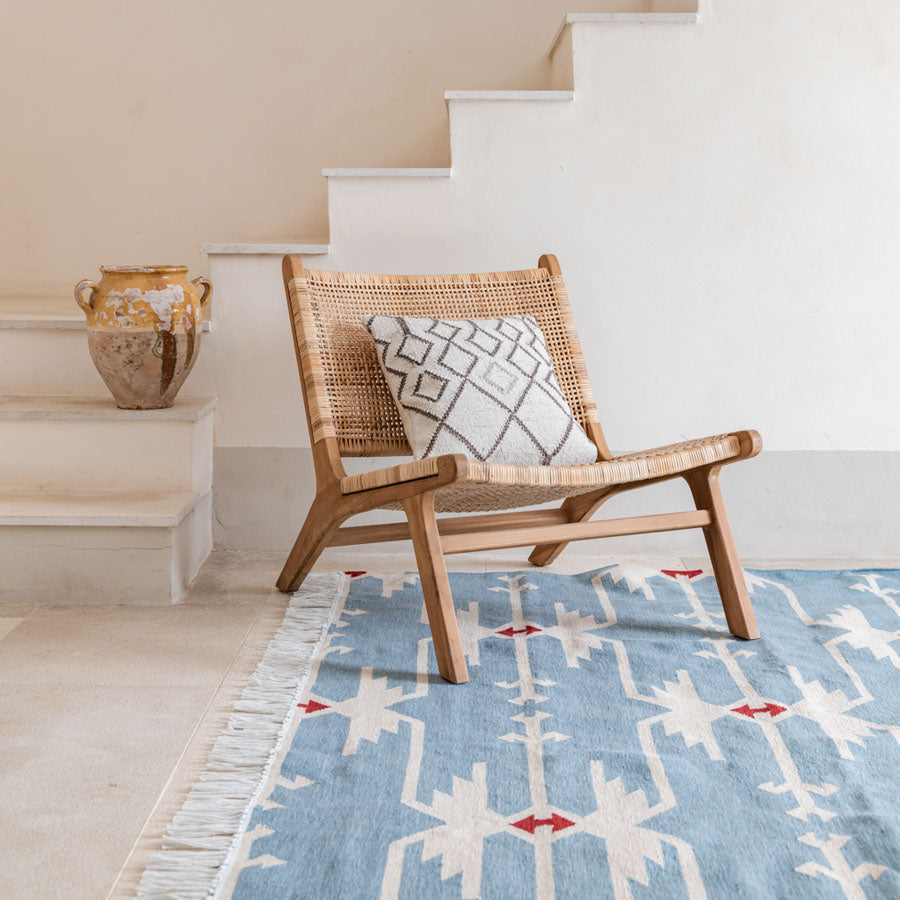 A Sky Blue colored rug with traditional geometric motifs placed in a room with a wooden chair and a decorative pillow, near a staircase.