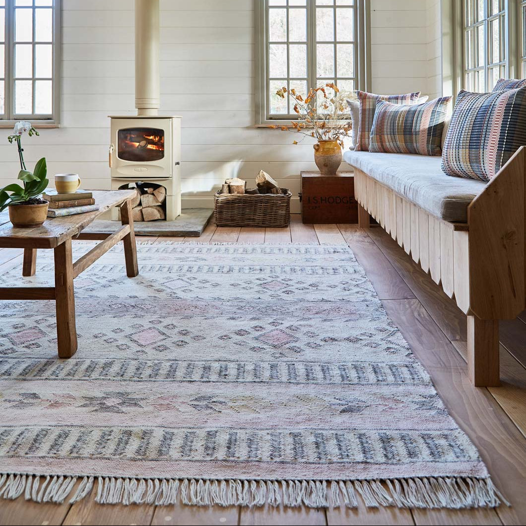 A well-lit room featuring a traditional Spanish inspired rug with natural tones in coral, pink, and charcoal, placed under a window near a wooden sofa and a fireplace.
