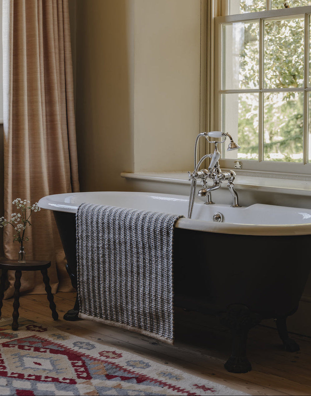 Freestanding bathtub with a towel draped over it in a room with a window and curtains.