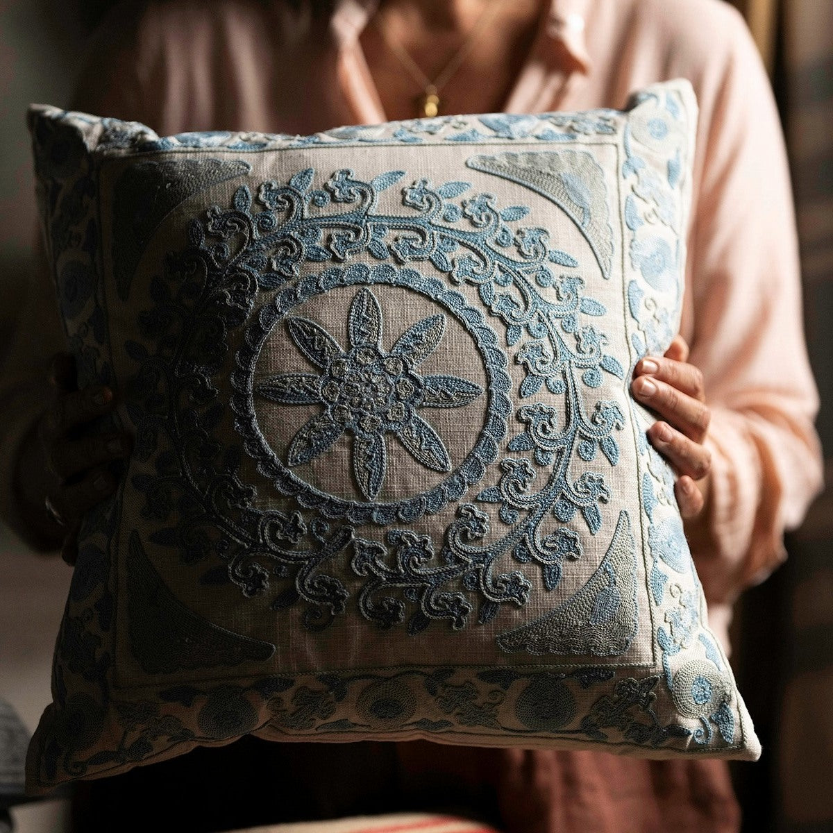 Person holding a blue embroidered cushion with intricate patterns.