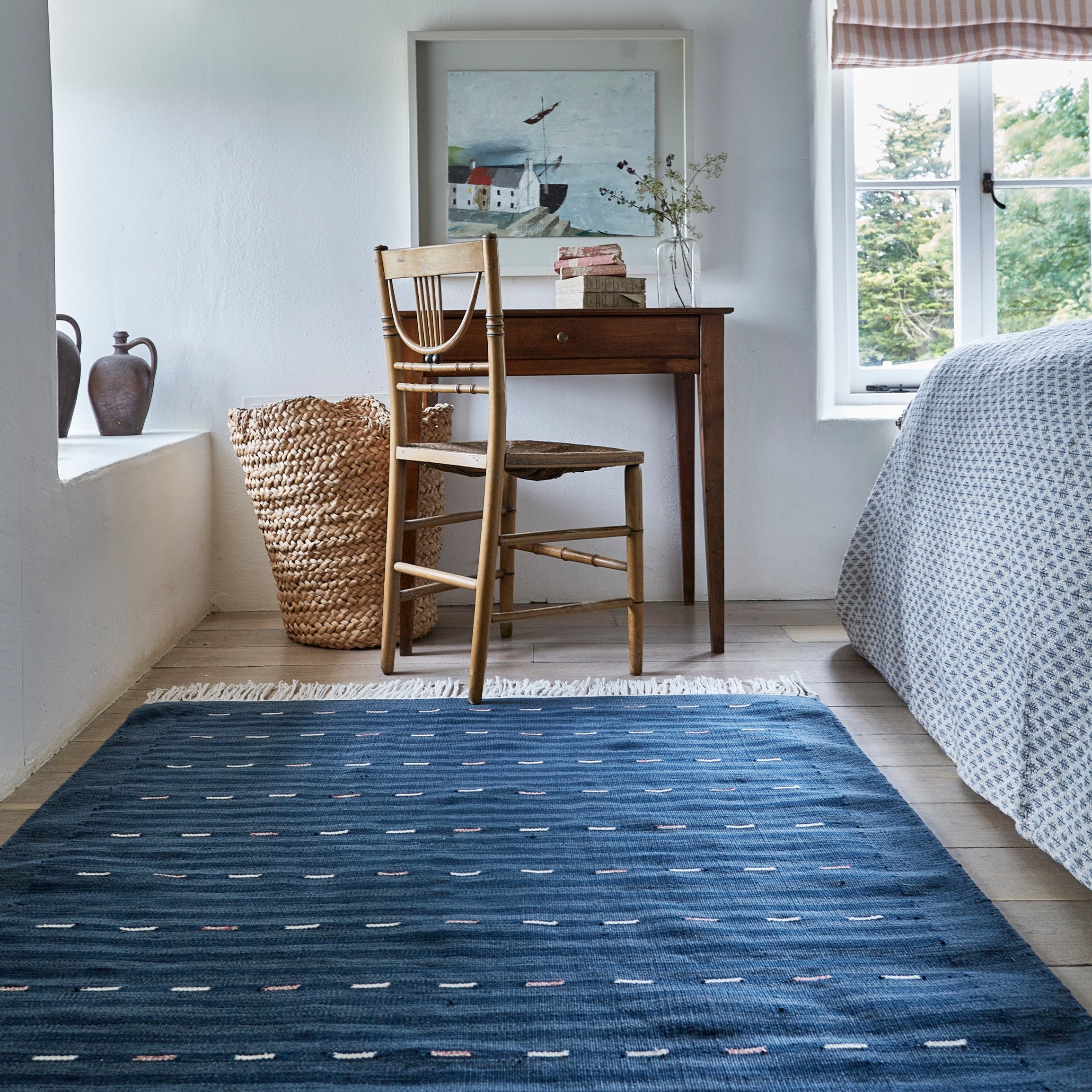 Room with a blue patterned rug, wooden chair, desk, and window with striped curtain.