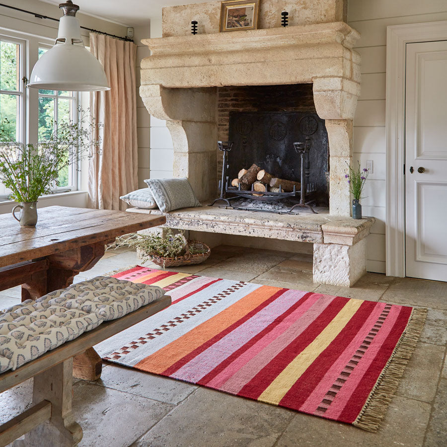 A multicolored striped rug with a boho style, featuring vibrant colors, laid out in a room with a fireplace and wooden furniture.