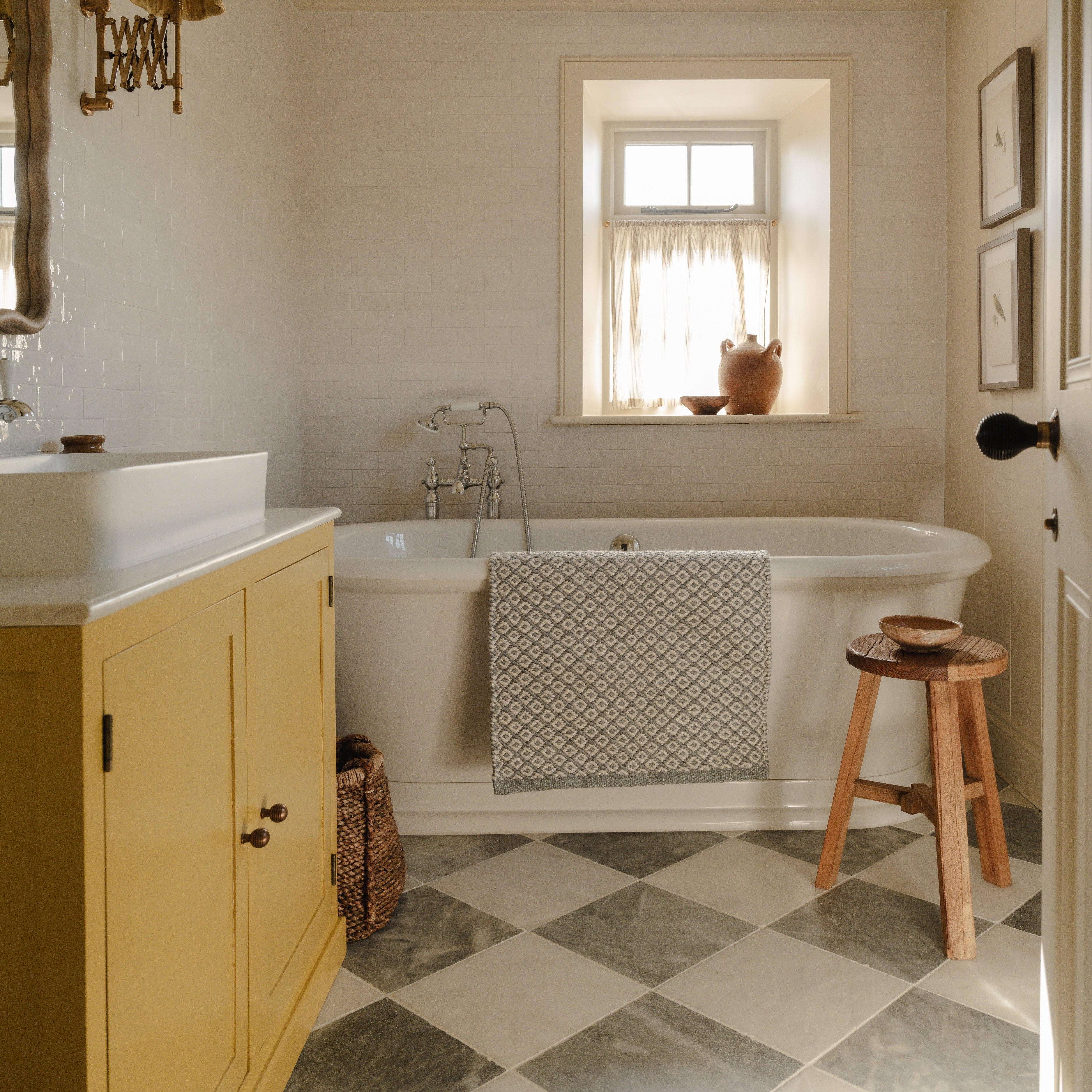 Bathroom with a bathtub, cabinet, and stool near a window.