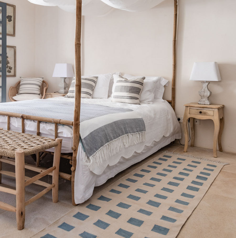 A runner rug with a geometric pattern in blue and beige colors, placed on a floor in a room with a bed and nightstand.