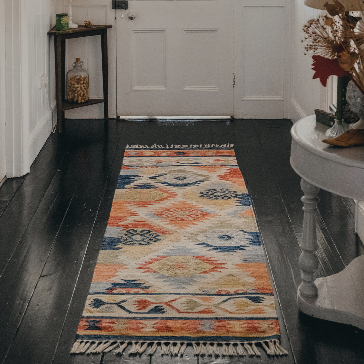Native American inspired runner rug with motif repeat, in blues, greens, corals and neutrals on a dark wooden floor with a white door in the background.
