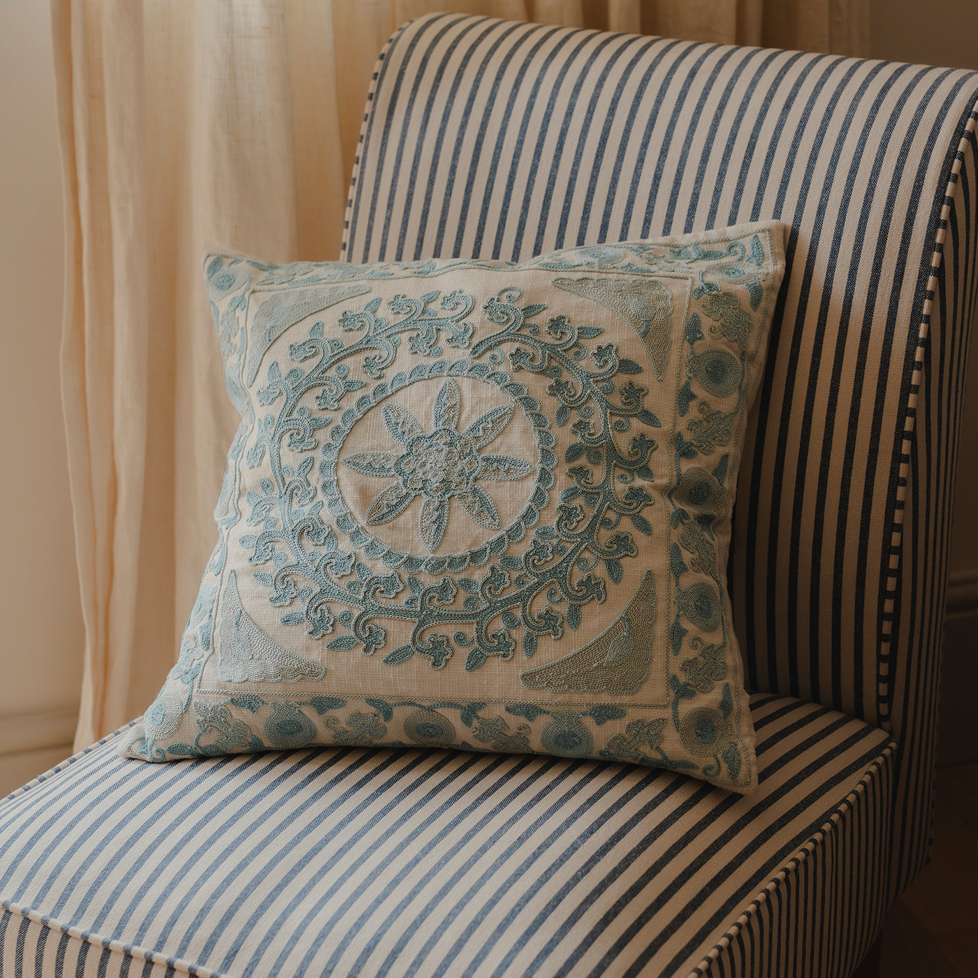 Blue embroidered cushion with a floral geometric design placed on a blue and white striped chair.