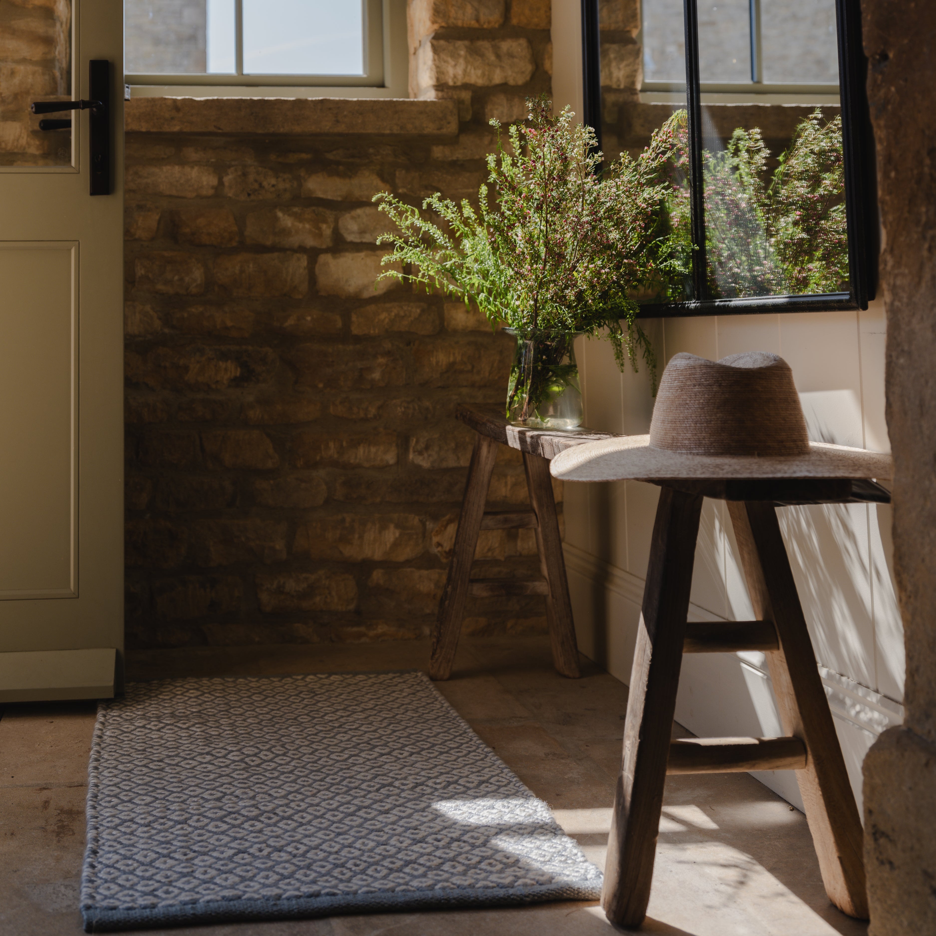 Nestled corner of a rustic room with stone walls, a rug, and a stool.