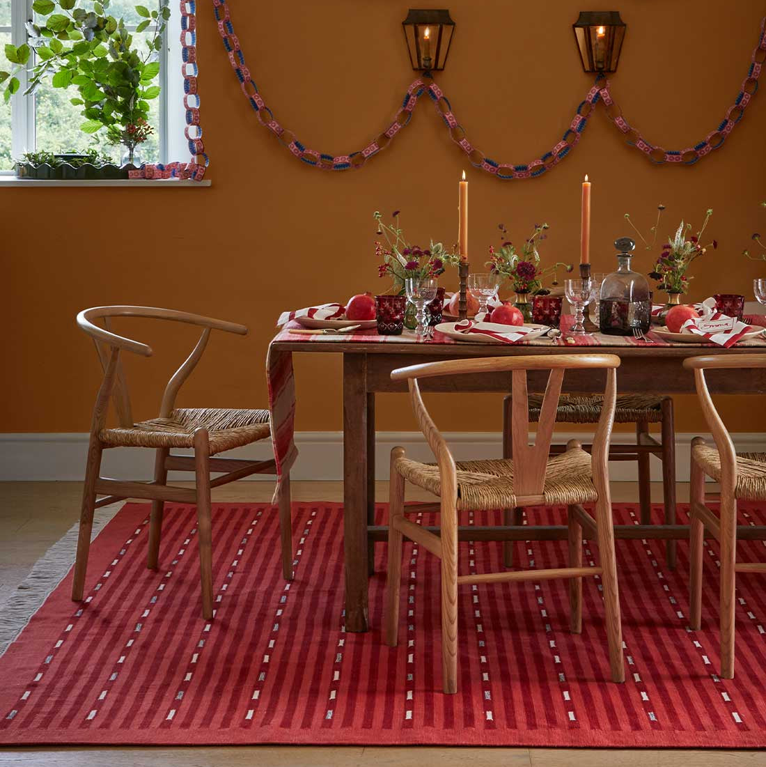 Dining room with a wooden table set for a meal, chairs, and a red rug.