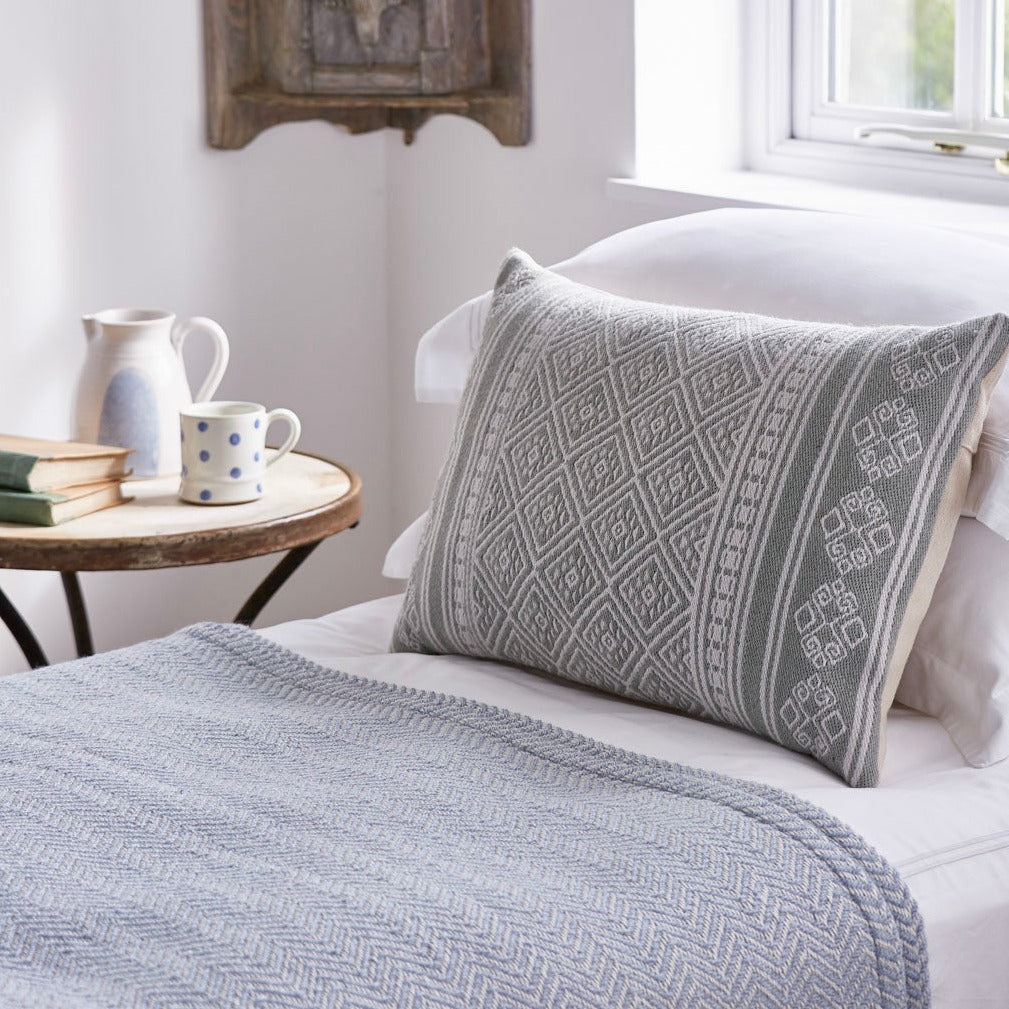 Embroidered cushions in grey green placed on a bed.