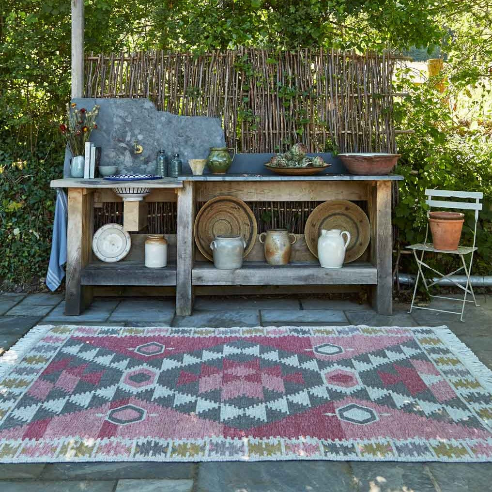 A geometric colourful rug outdoors in the garden with trees on a stone patio.