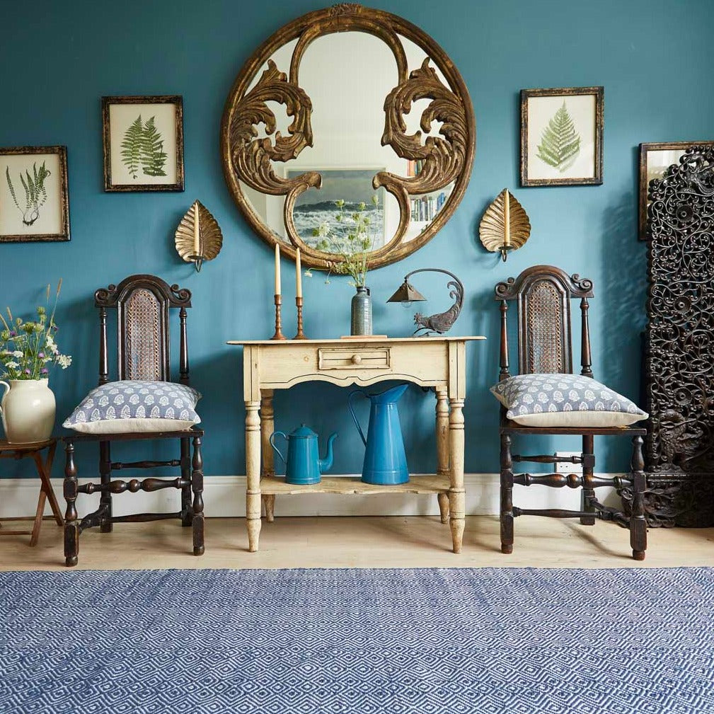 A navy blue diamond pattern rug placed under a wooden table and chairs in a room with blue walls and decorative mirrors.