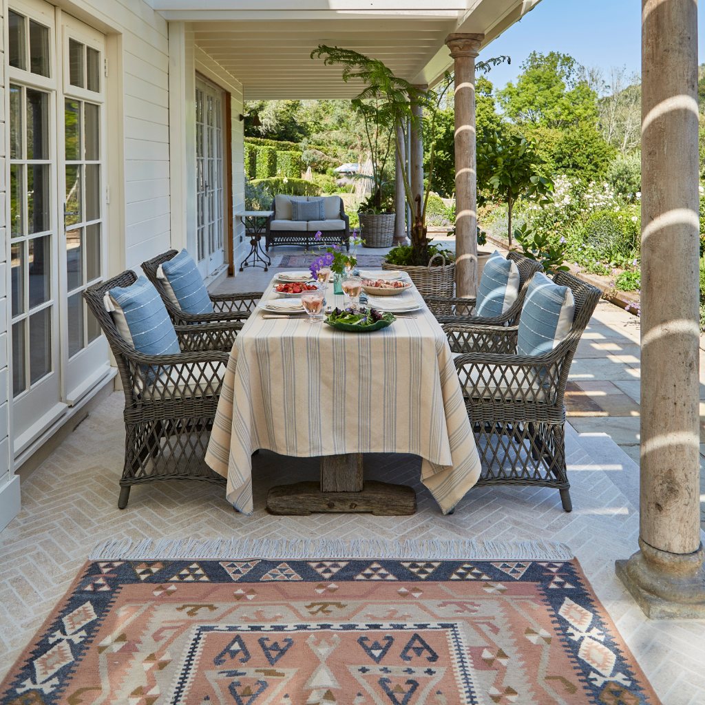 Outdoor patio with table set for a meal, chairs, and Weaver Green's Aster Kilim patterned rug.