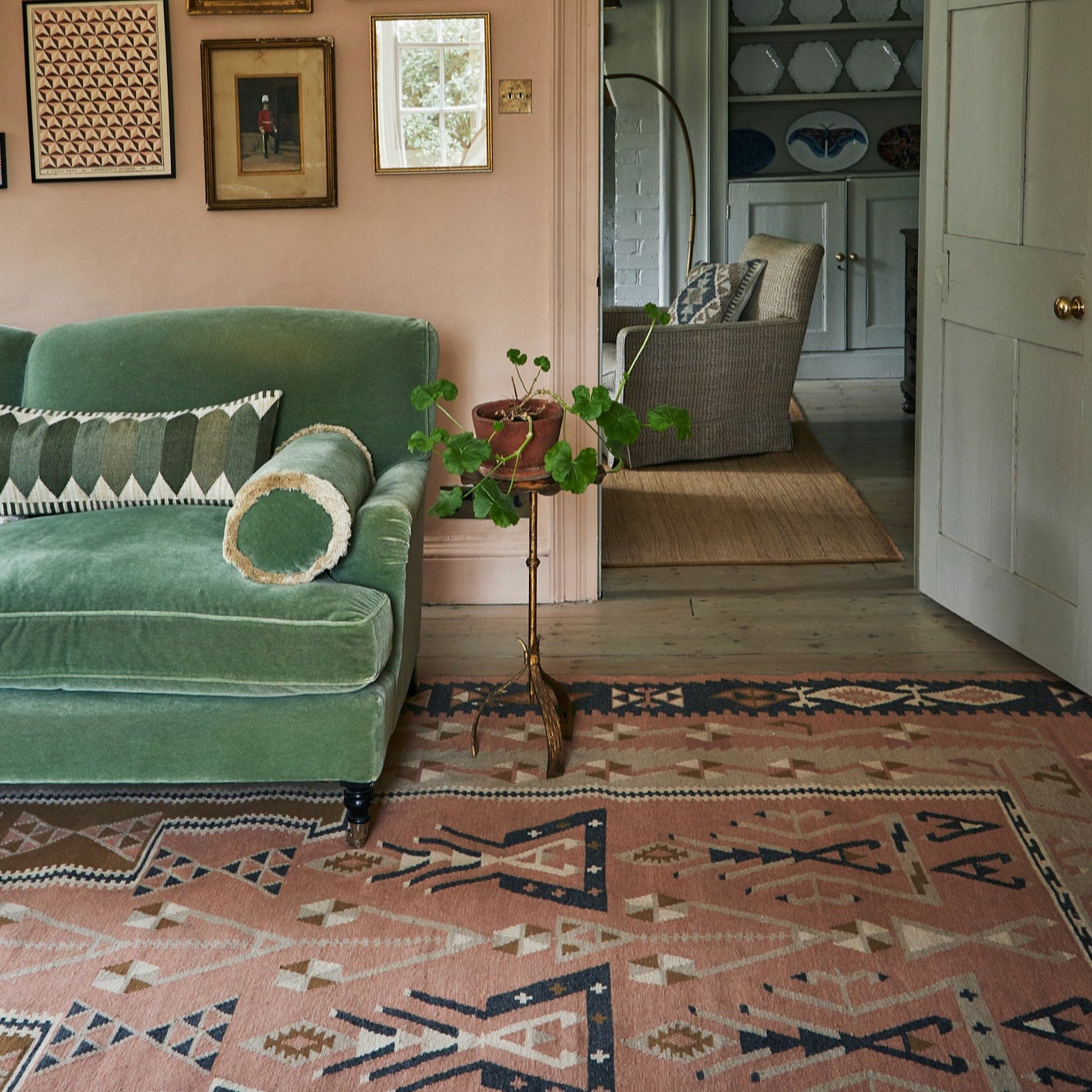 Living room with green sofa, patterned kilim pink rug, and framed pictures on the wall.