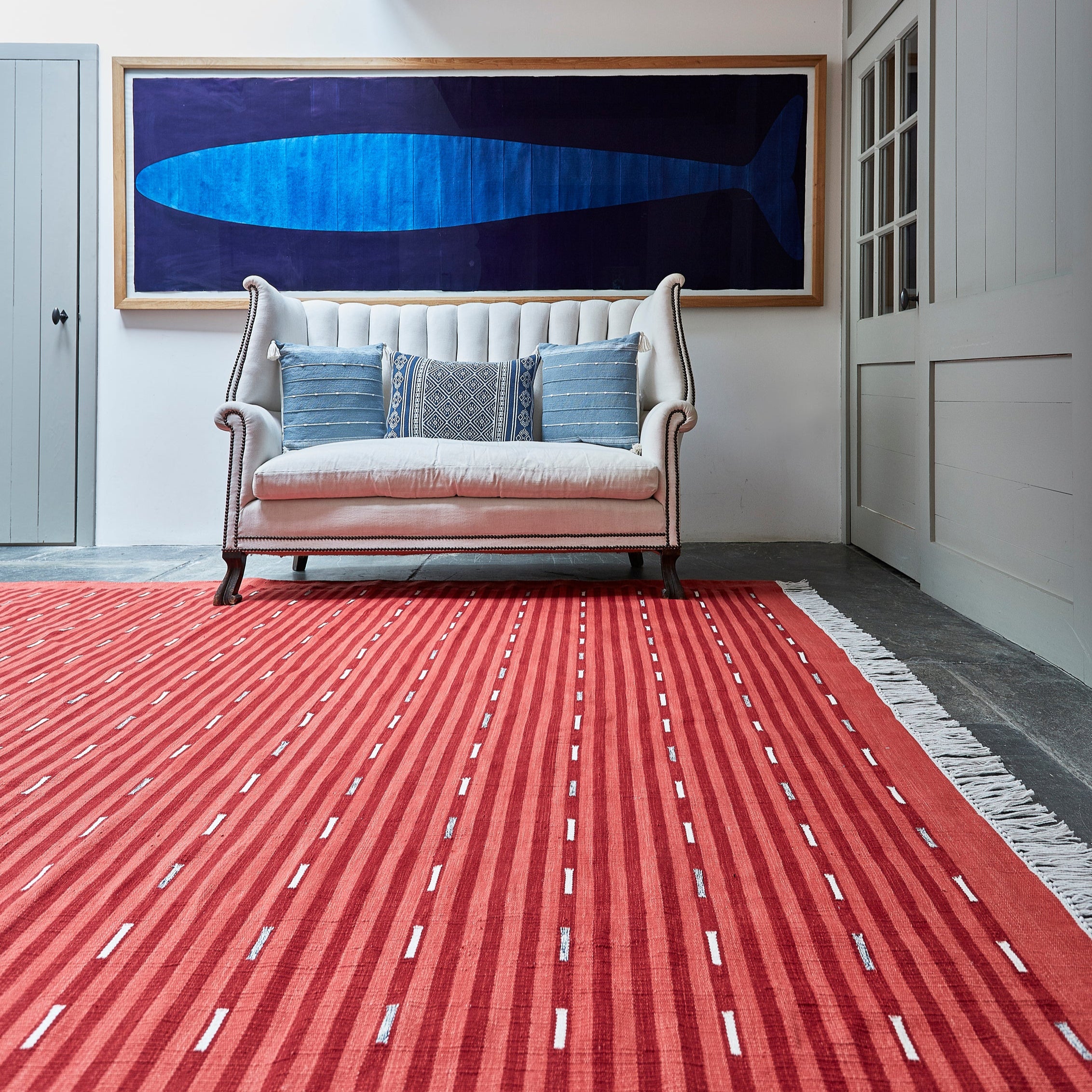 Living room with a red patterned rug, white sofa, and blue abstract painting on the wall.