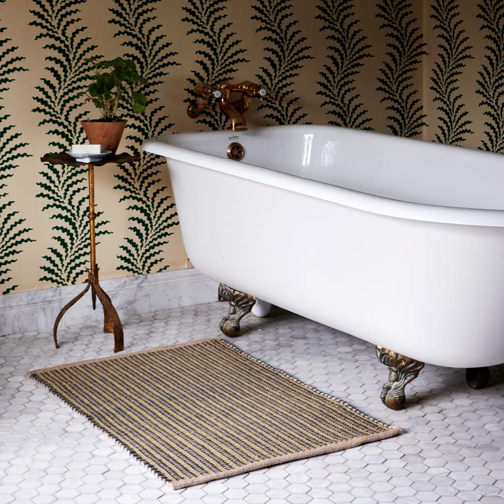 Bathroom with a freestanding bathtub, striped rug, and decorative wall paper.
