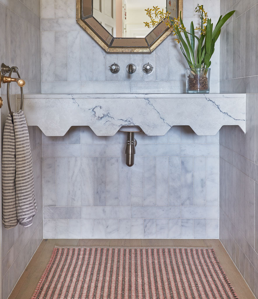 A hand-woven rug with a striped pattern in coral and charcoal colors, under the sink in a marble bathroom 