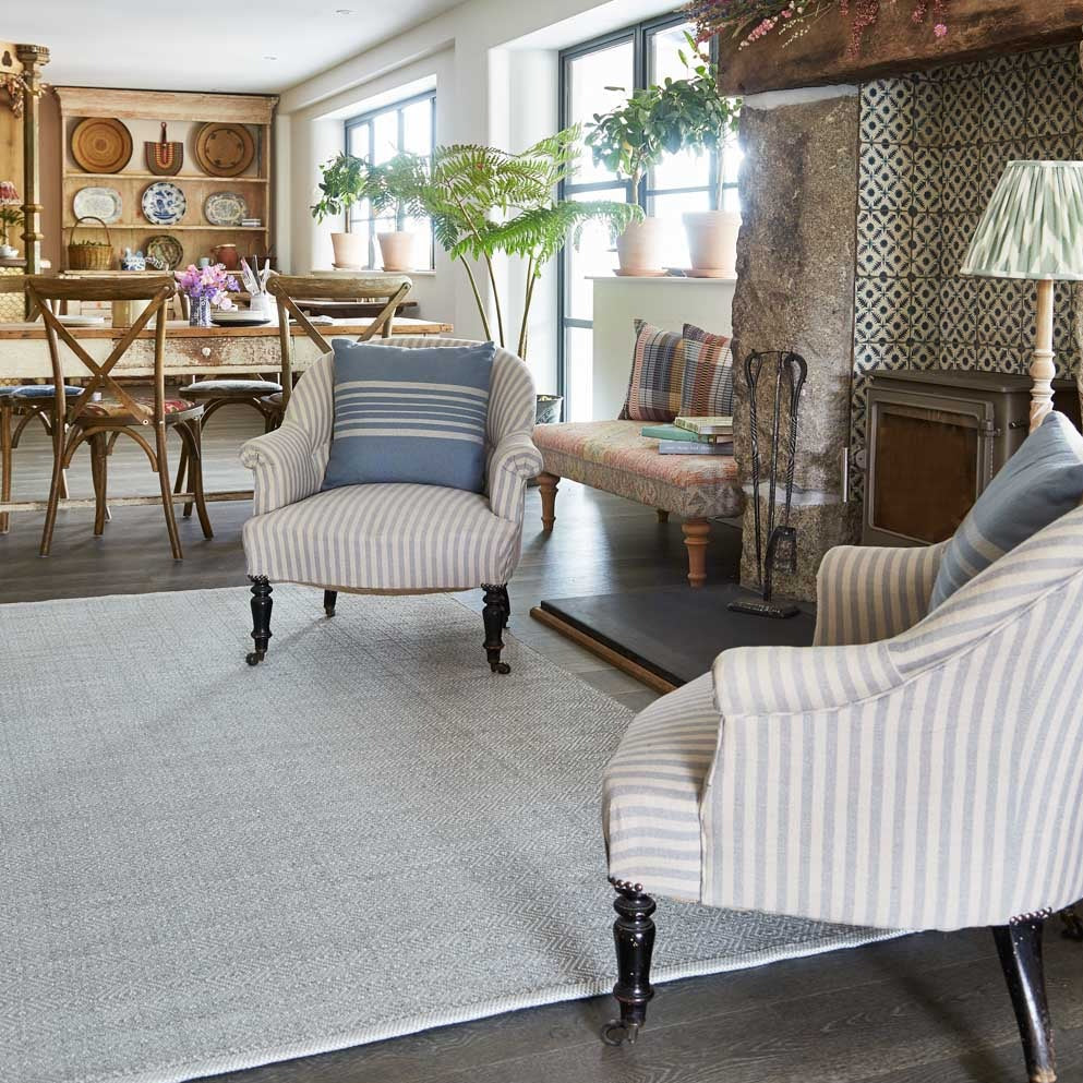 A dove grey rug with a subtle diamond pattern, placed under a chair and a table in a cozy living room setting.
