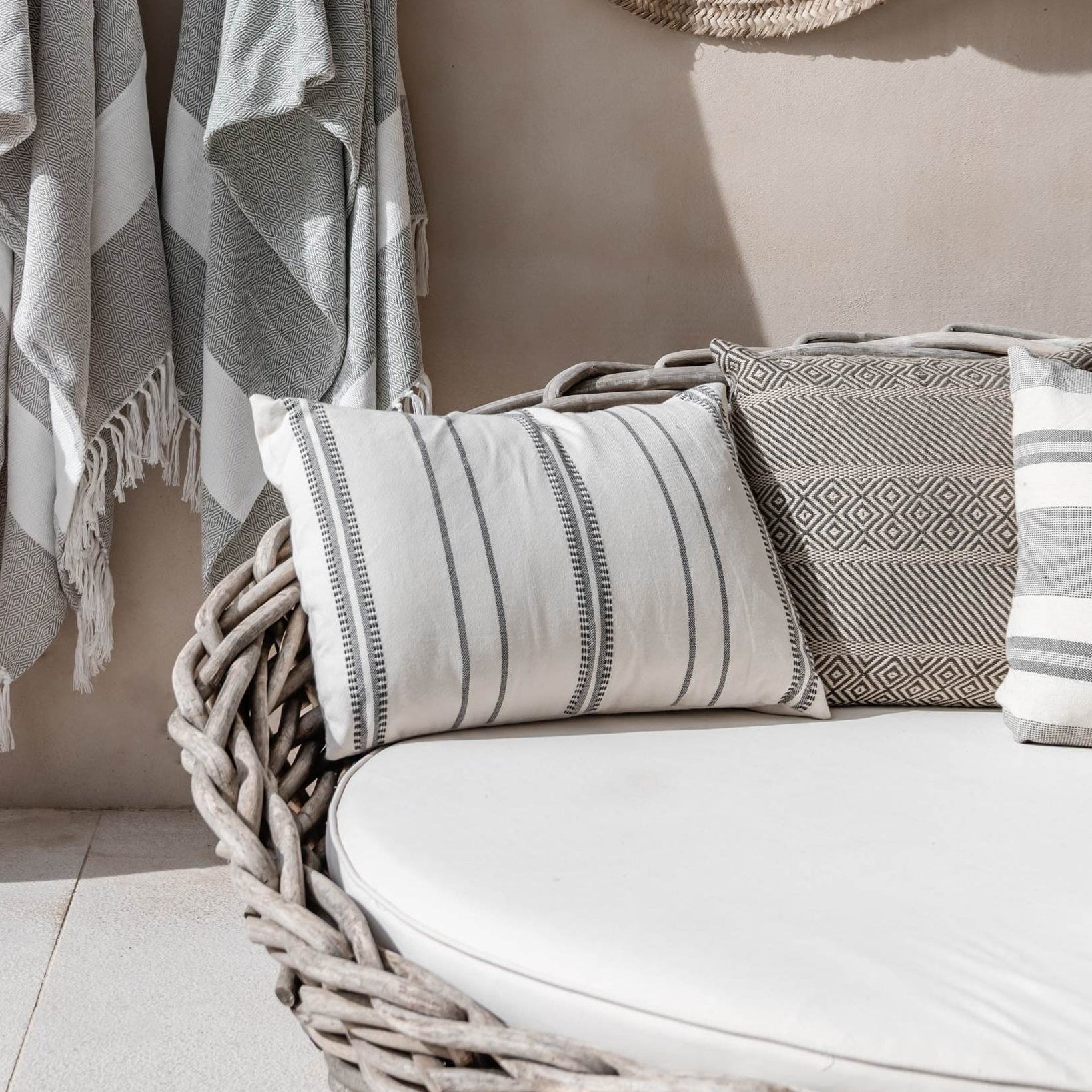 Towels, a hat, and a bag hanging on hooks against a beige wall with a wicker chair and a Las Salinas Cushion.